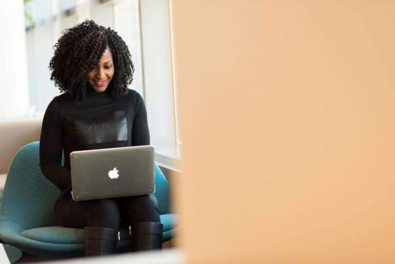 African American woman happily working on a laptop in a modern office setting.